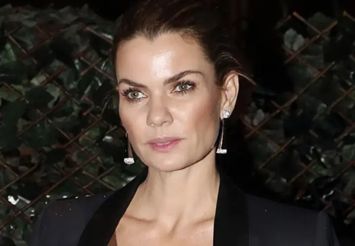 Alejandra de Rojas, con pendientes largos y un blazer negro, posa con una mirada intensa frente a un fondo de vegetación.