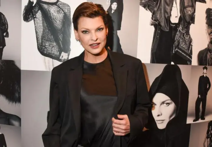 Linda Evangelista hoy, posando con confianza frente a un collage de sus icónicas fotos de moda.