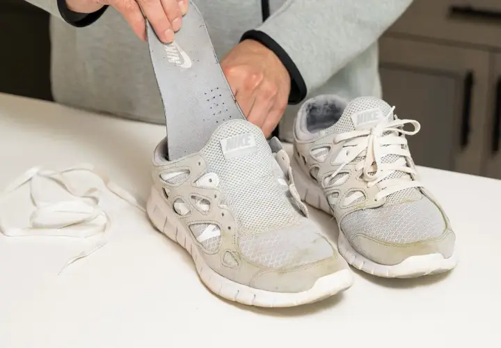 Man removes insole from dirty white Nike sneakers. Learn como quitar desteñido en zapatillas blancas.