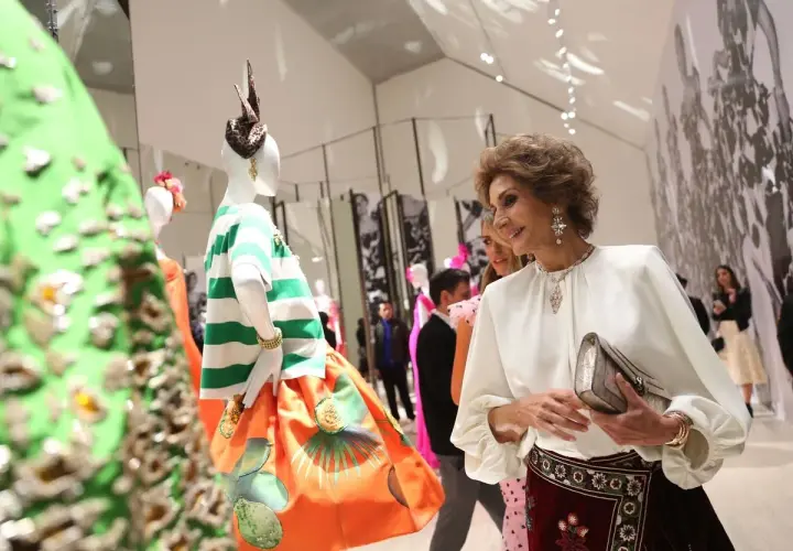 Naty Abascal, elegante y sonriente, admira creaciones de moda en una exposición.
