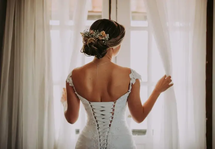 Novia con un juvenil recogido de boda adornado con flores, luciendo su espalda con un corsé de encaje.