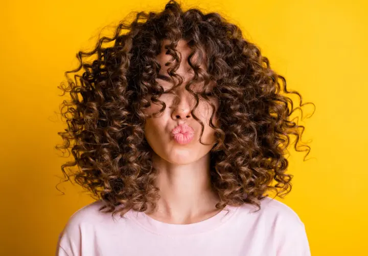 Mujer con pelo corto rizado y labios en forma de beso, sobre fondo amarillo.