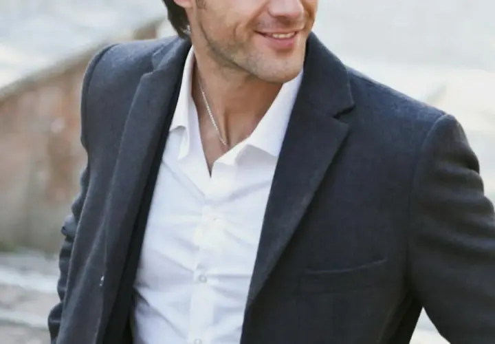 Hombre sonriente con chaqueta gris y camisa blanca, luciendo un estilo look smart casual.