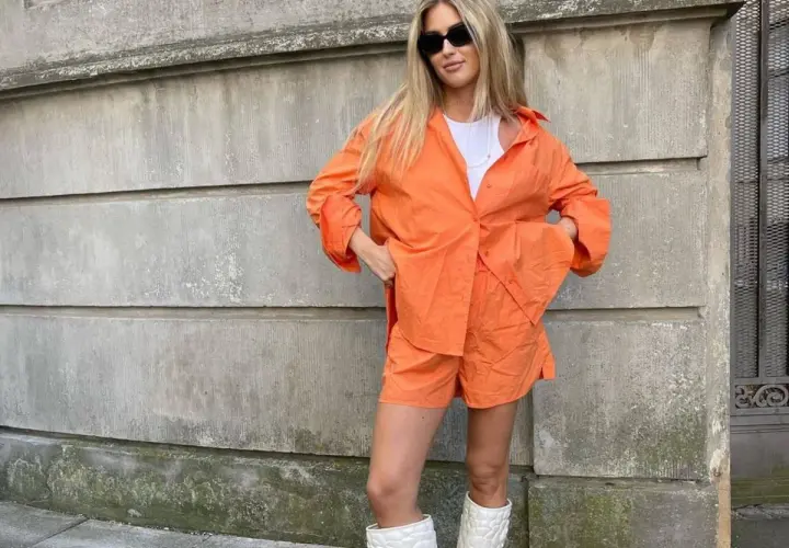Mujer con conjunto naranja, gafas de sol y botas blancas. Se ve muy comfy y lista para pasear.