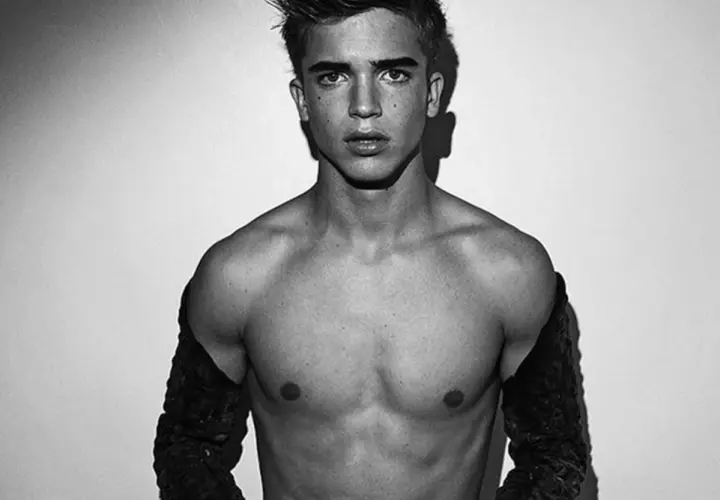 Joven modelo hombre con mirada intensa, torso descubierto y mangas oscuras.