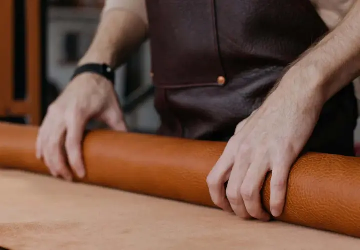 Manos de artesano desenrollando un rollo de cuero, mostrando la textura y el color natural del material. Se pregunta de que esta hecho el cuero.