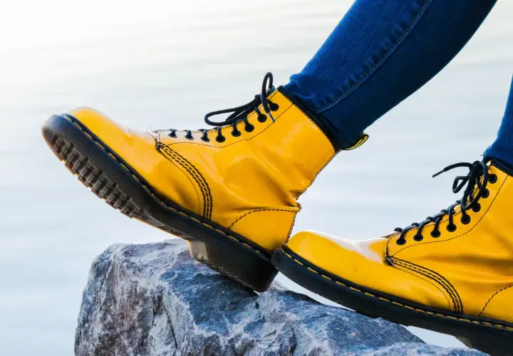 Botas amarillas de charol, con cordones negros, pisan una roca. Las botas de piel ceden ante la aventura.