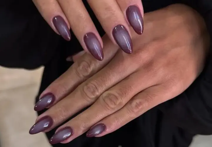 Manicura con uñas almendradas en tono morado oscuro, con un efecto degradado que recuerda a las aura nails.