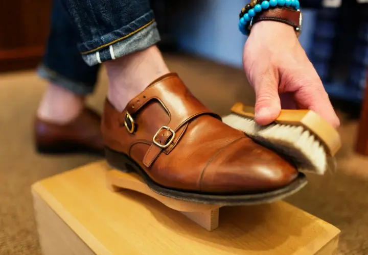 Hombre cepillando un zapato de piel marrón, parte de como limpiar zapatos de piel.