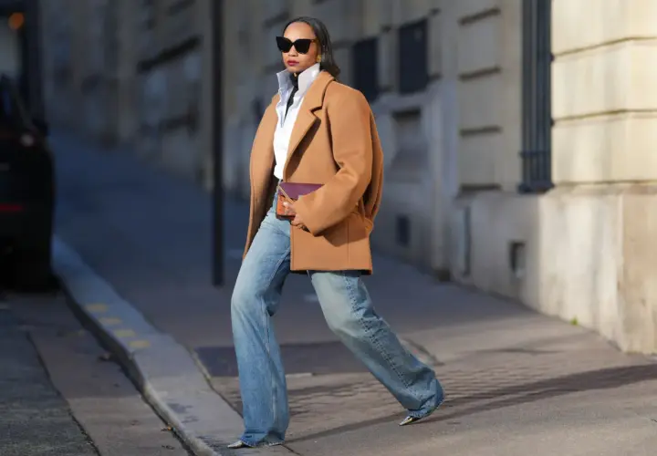 Mujer con abrigo camel, camisa blanca y jeans anchos, luciendo un bolso morado. Su estilo es muy aesthetic.