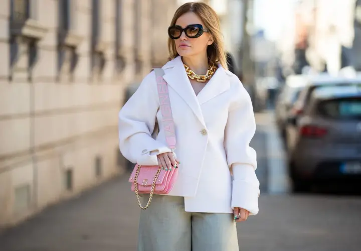Look para mujeres de 50 años bajitas: abrigo blanco, pantalón verde, bolso rosa y cadena dorada.