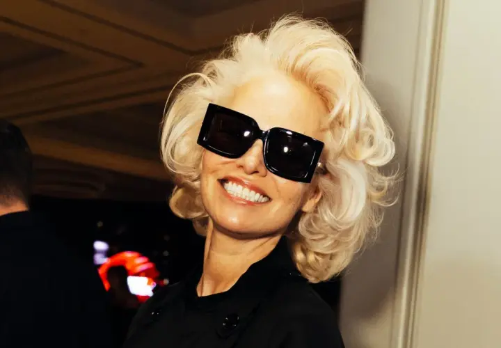 Pamela Anderson, con su icónica melena rubia y gafas de sol XL, sonríe con confianza.