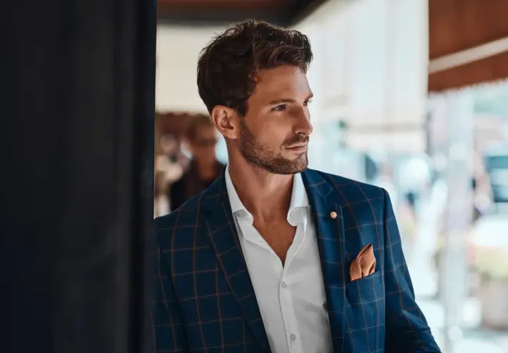 Un invitado boda hombre sin traje, con chaqueta a cuadros, camisa blanca y pañuelo naranja.
