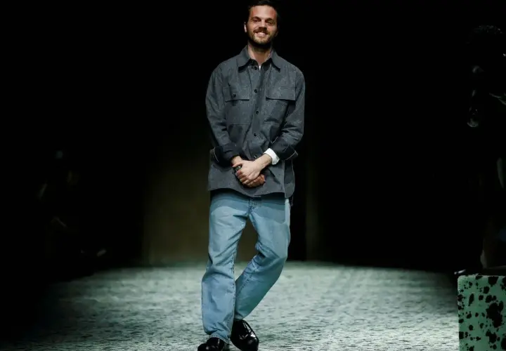 Matthieu Blazy, diseñador de Bottega Veneta, sonríe en la pasarela con camisa gris y vaqueros.