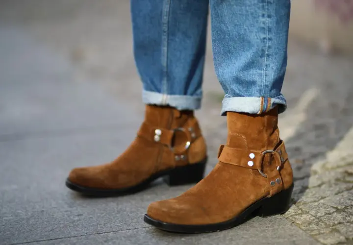 Botas de gamuza marrón con hebillas y jeans doblados. La piel girada de las botas contrasta con el denim.