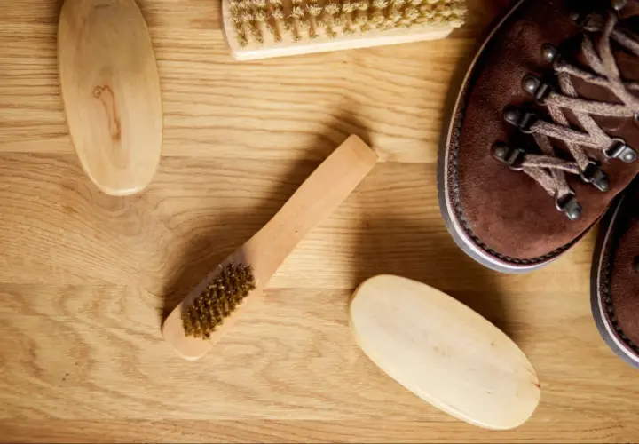 Cepillos y bota de piel de ante marrón sobre madera.