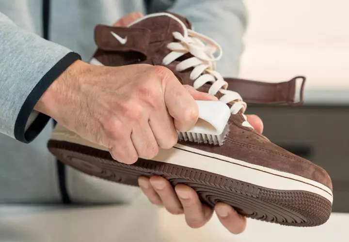 Man limpiando serraje de una zapatilla marrón con un cepillo blanco.