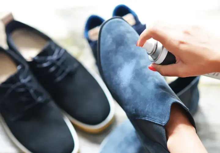 Aplicando spray protector a unas botas de terciopelo azul. Aprende como limpiar botas de terciopelo para mantenerlas como nuevas.