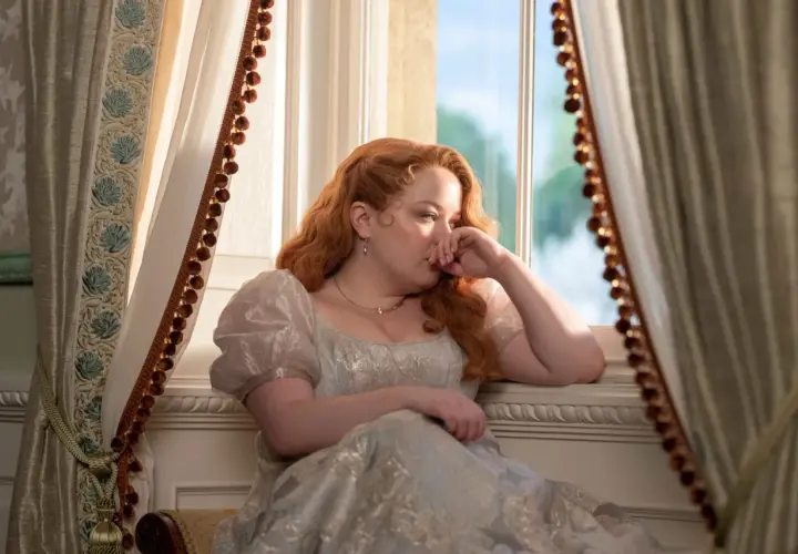 Penelope Bridgerton, la actriz, reflexiona junto a la ventana con un vestido de época.