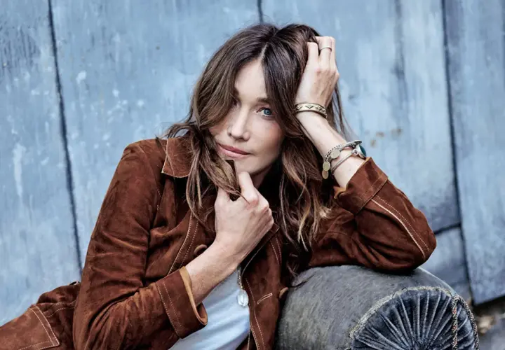 Carla Bruni joven, con su melena suelta y mirada penetrante, posa con una chaqueta de ante marrón.