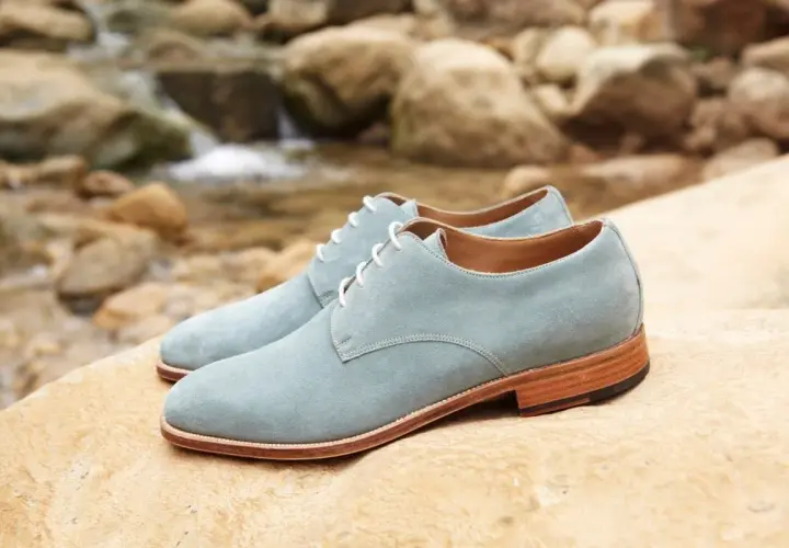 Zapatos de ante azul claro con cordones blancos, descansando sobre rocas junto a un arroyo. ¡Qué ante en zapatos!