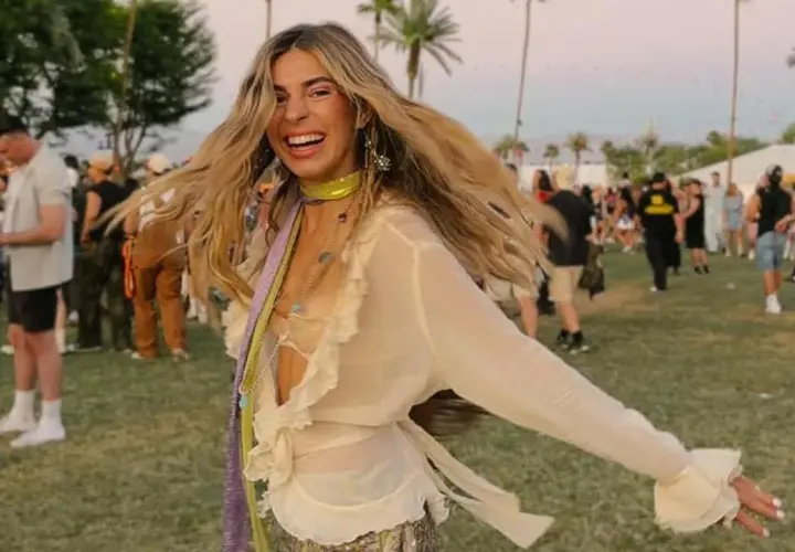 Mujer sonriente y con el pelo al viento disfruta de un look festival verano, rodeada de palmeras y gente.