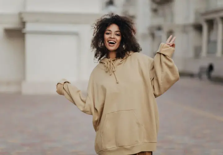 Mujer sonriente con pelo rizado, luciendo un cómodo estilo oversize en sudadera beige.