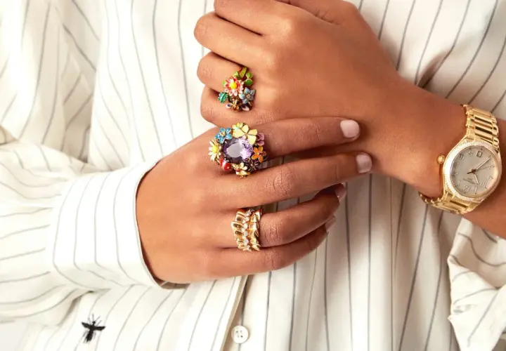 Manos adornadas con anillos florales coloridos y un reloj dorado, luciendo un estilo suot studio.