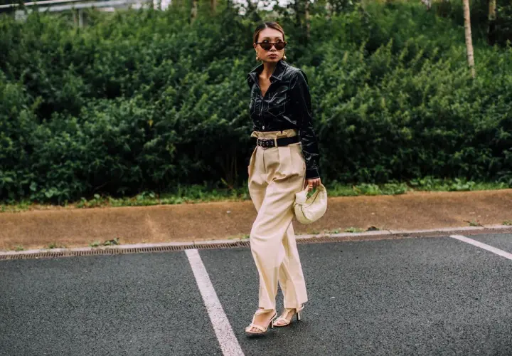 Mujer con elegante **pantalón beige** de talle alto, camisa negra brillante y bolso blanco.