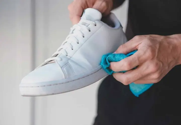 Manos limpiando las gomas de unas zapatillas blancas con un paño azul. Un detalle para saber como limpiar las gomas de las zapatillas y dejarlas como nuevas.