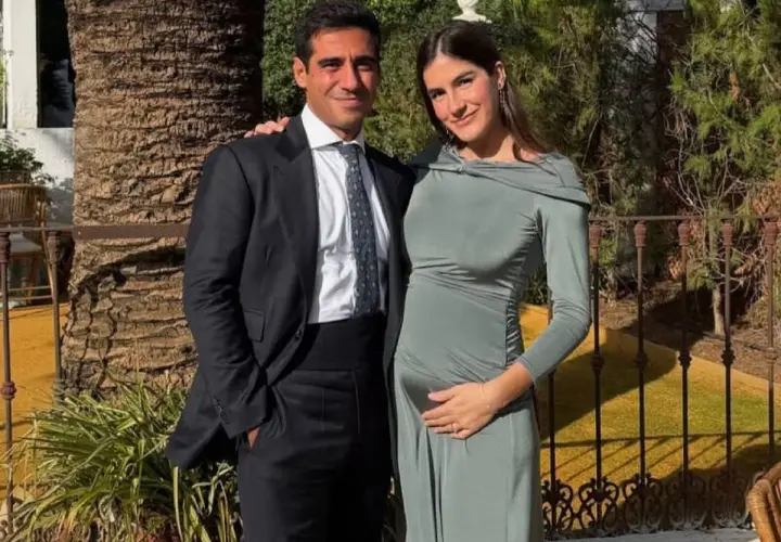 Pareja sonriente, él con traje oscuro, ella con vestido verde ceñido, acariciando su vientre. Blanca Llandres, radiante, espera un bebé.