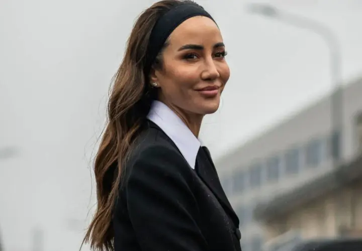 Mujer con peinado con diadema y pelo suelto, luciendo un traje negro y camisa blanca.