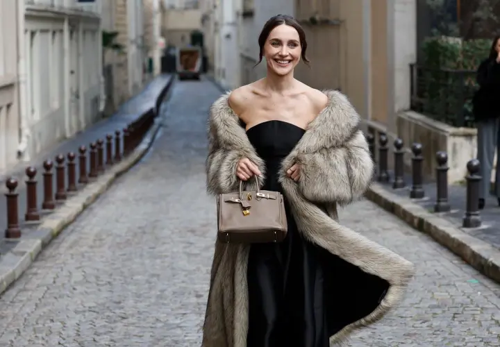Elegante mujer con abrigo de pelo y bolso, lista para una boda en otoño.