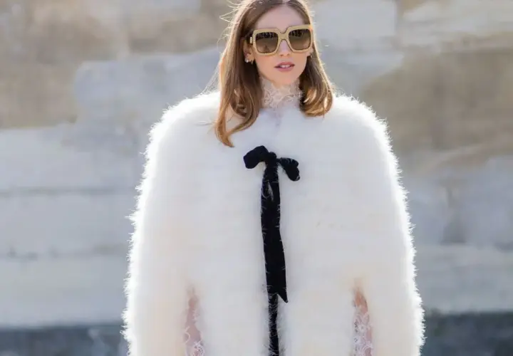 Estilo maximalismo: mujer con abrigo blanco de pelo, gafas grandes y lazo negro.