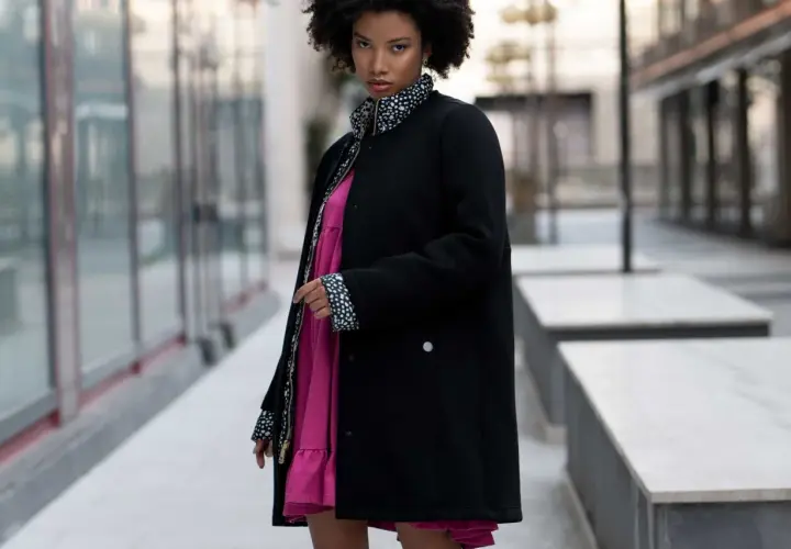 Mujer con estilo urbano y moda oversize, luce un vestido rosa vibrante bajo una chaqueta negra con detalles de lunares.