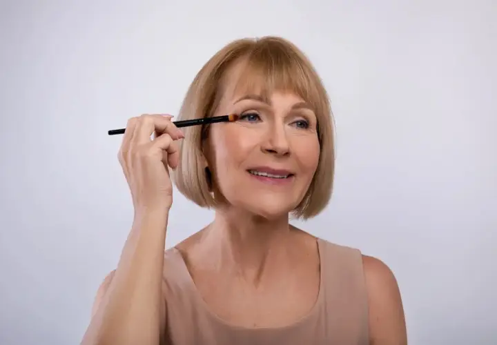Mujer mayor aplicando sombra de ojos con brocha, aprendiendo como maquillar los ojos a partir de los 50 años para realzar su belleza natural.