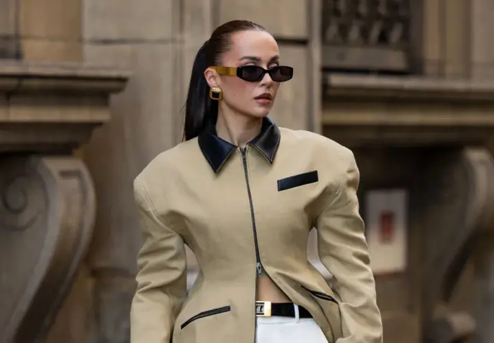Mujer con gafas de sol y chaqueta beige con cuello negro, luciendo un look de street style impecable.