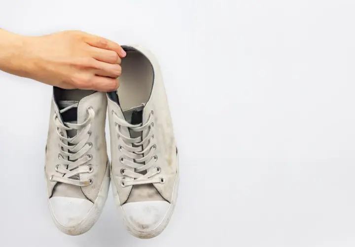 Mano sosteniendo un par de zapatillas blancas de tela sucias, listas para limpiar.