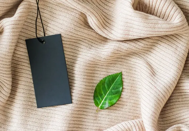 Etiqueta negra sobre tejido beige, con una hoja verde al lado. Símbolo de una marca sostenible.