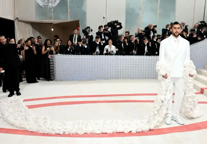 Bad Bunny deslumbra en la Met Gala con un traje blanco adornado con flores, rodeado de fotógrafos.
