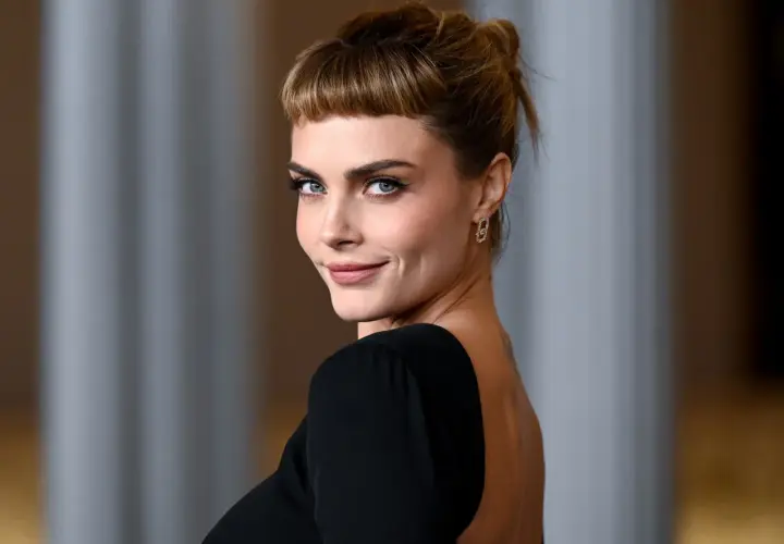 Cara Delevingne, con su mirada penetrante y un peinado recogido con flequillo, luce un elegante vestido negro de espalda descubierta.