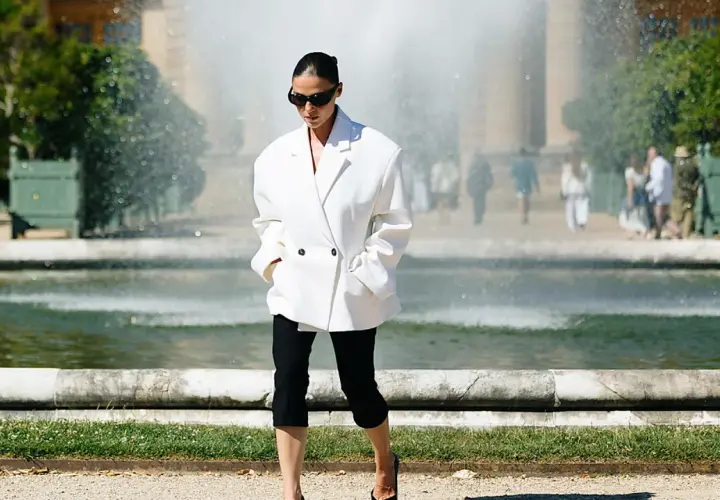 Mujer con un elegante outfit con leggins negro y blazer blanco, paseando cerca de una fuente.
