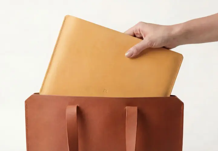 Mano colocando un portátil de piel vegetal en un bolso de cuero.
