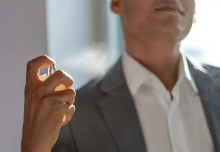 Hombre aplicándose perfume con un frasco rociador.