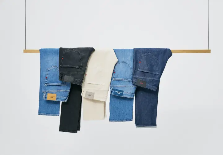 Cinco tipos de pantalones, incluyendo vaqueros azules, negros y beige, colgados en una barra de madera.