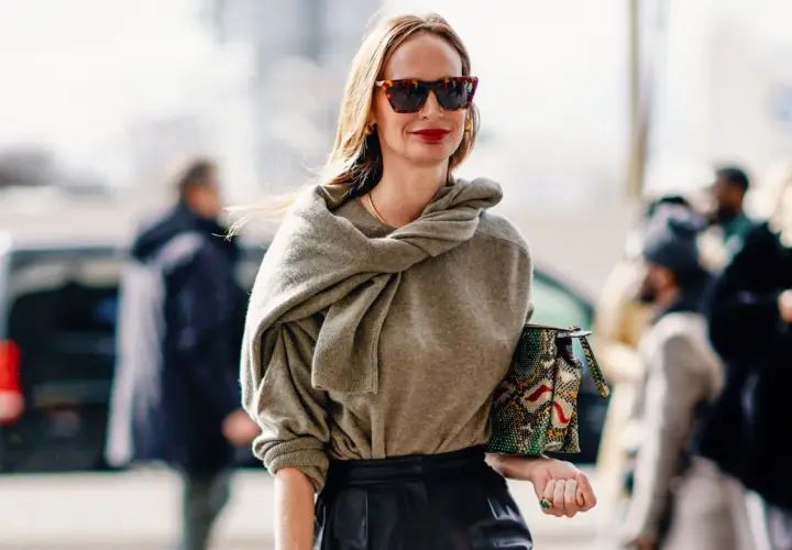 Mujer de unos 40 años con un look casual chic, gafas de sol, suéter gris y bolso estampado.