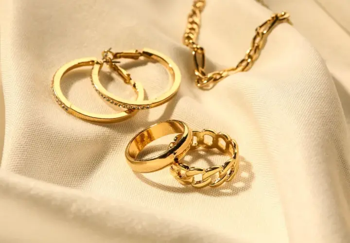 Anillos y cadena dorados sobre tela. Los aros tienen pequeñas piedras preciosas incrustadas, como si fueran diamantes.