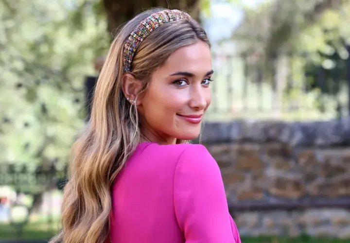 María Pombo, con un llamativo tocado de pedrería y un vestido fucsia, sonríe mirando por encima del hombro.