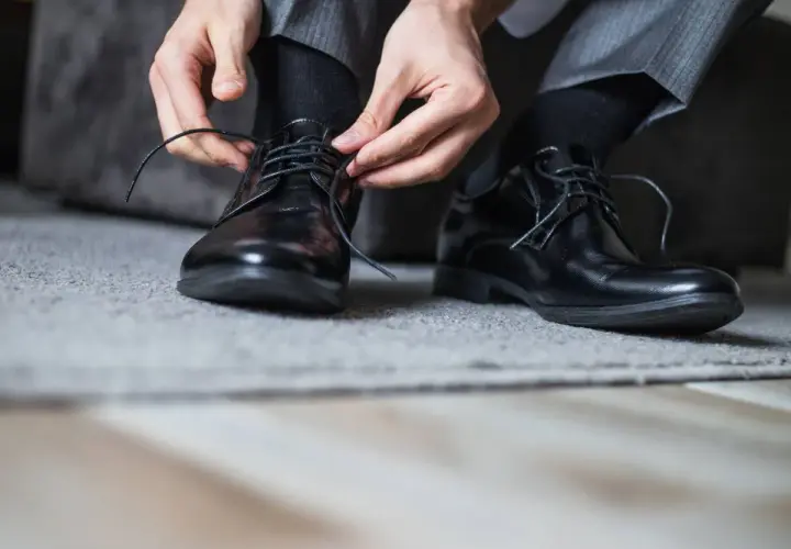 Man se ata los cordones de sus zapatos de piel negros, preparándose para evitar rozaduras.