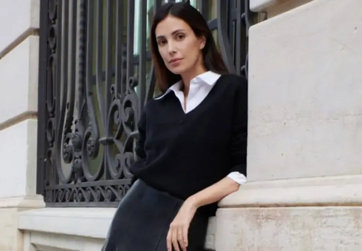 Sassa de Osma, elegante con jersey negro y falda de cuero, apoyada en una columna de piedra junto a una reja ornamental.